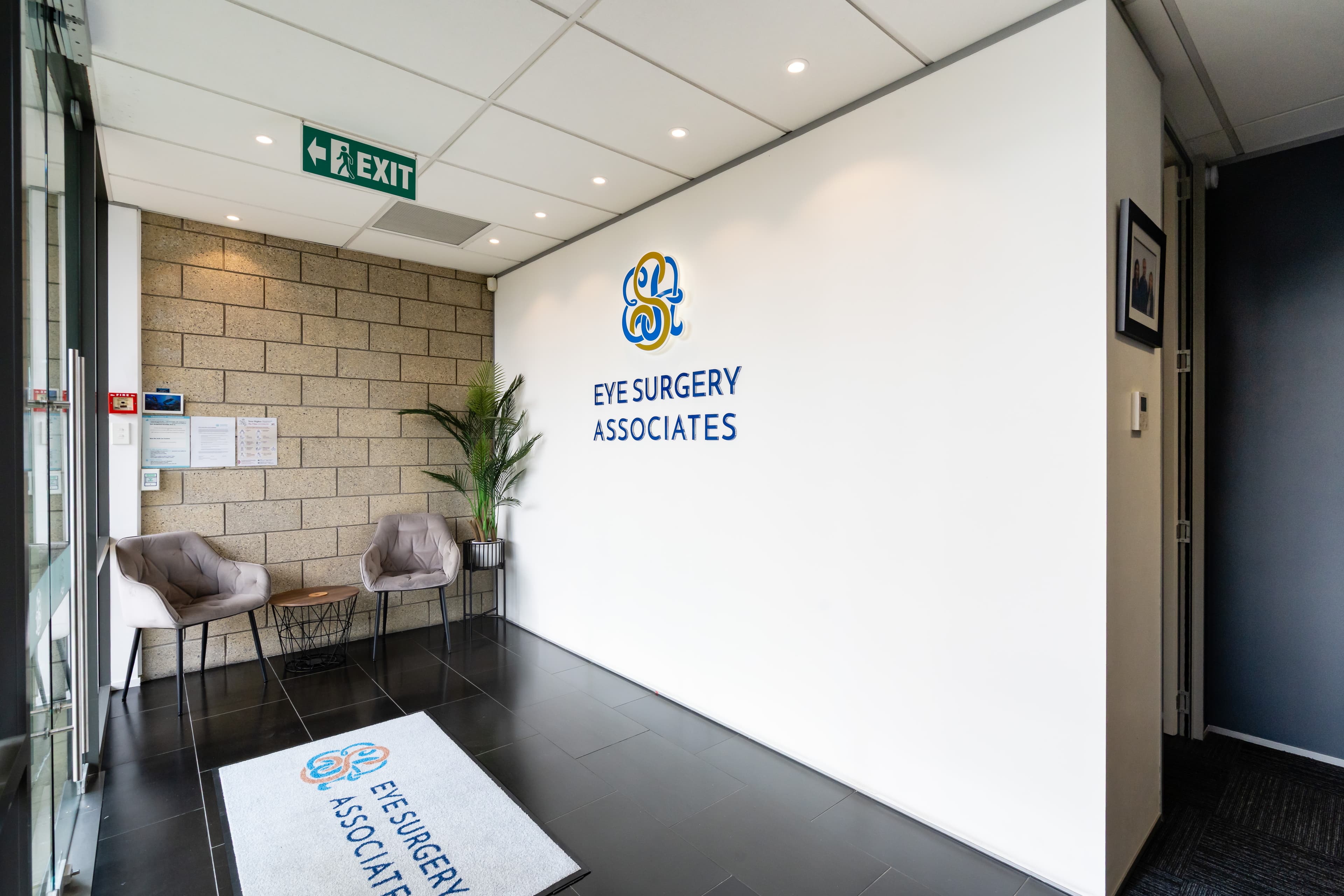 The clinic foyer, with seating against a brick wall beside the Eye Surgery Associates sign